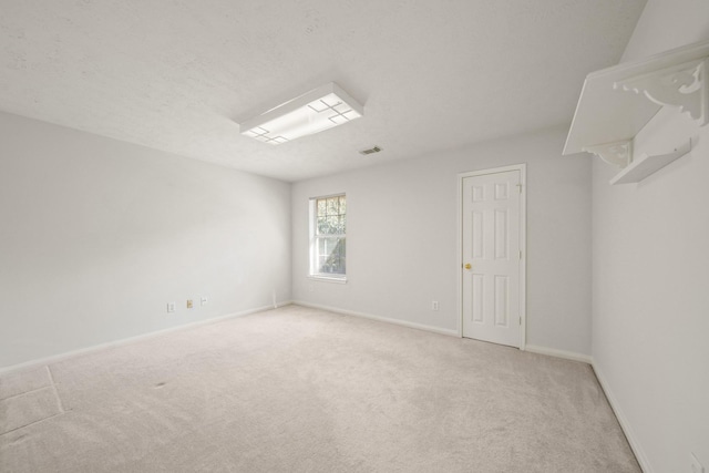 spare room with baseboards, a textured ceiling, and light colored carpet