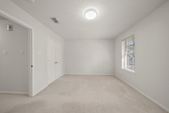 spare room with baseboards, visible vents, and light colored carpet