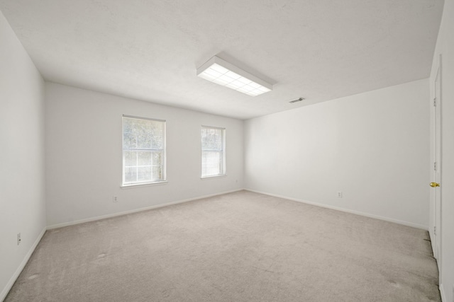 spare room with baseboards, visible vents, and light colored carpet