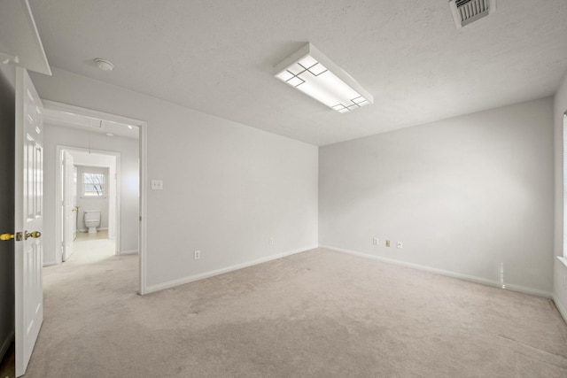 empty room with visible vents, attic access, light carpet, a textured ceiling, and baseboards