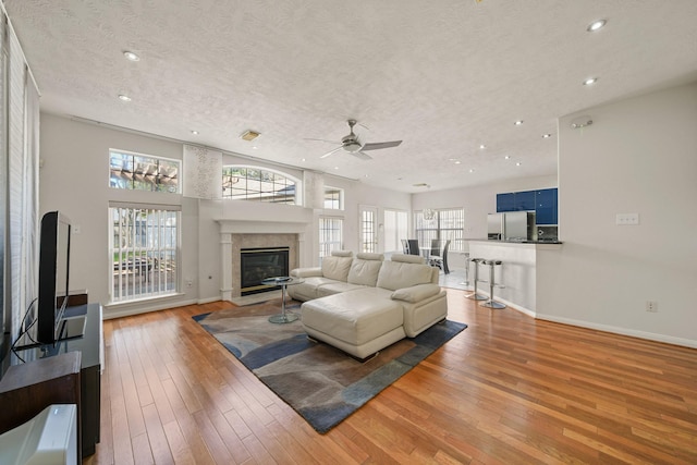 living room featuring baseboards, a glass covered fireplace, wood finished floors, a textured ceiling, and recessed lighting