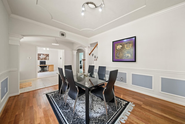 dining space with arched walkways, wood finished floors, visible vents, ornamental molding, and decorative columns