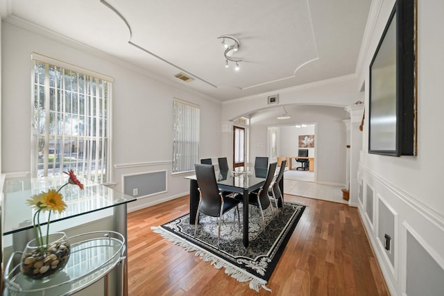 dining room with arched walkways, visible vents, crown molding, and wood finished floors