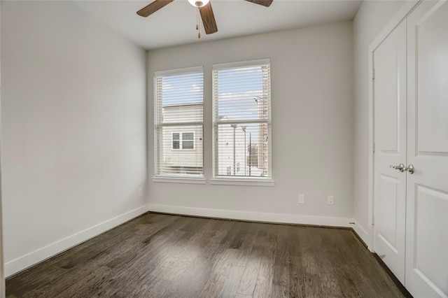 unfurnished room with dark wood-type flooring, a ceiling fan, and baseboards