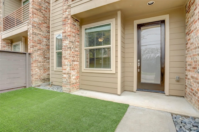 doorway to property featuring a lawn and brick siding