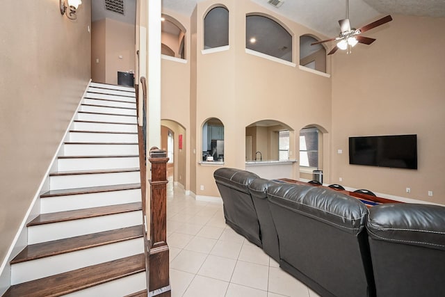 living area with arched walkways, light tile patterned flooring, visible vents, a ceiling fan, and stairs