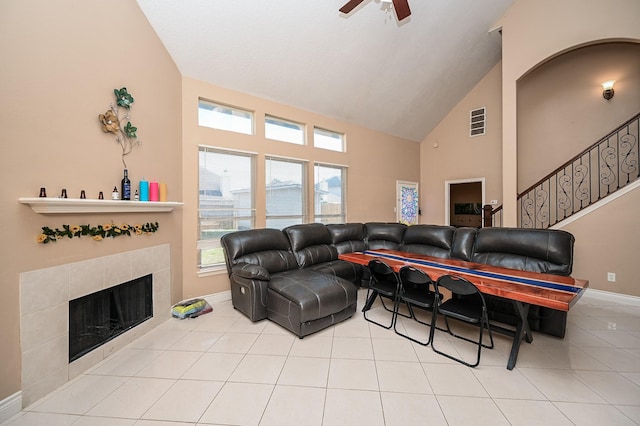 living area with light tile patterned floors, baseboards, a tile fireplace, stairway, and high vaulted ceiling