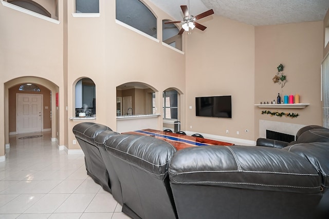 living room featuring light tile patterned floors, baseboards, arched walkways, a textured ceiling, and a fireplace