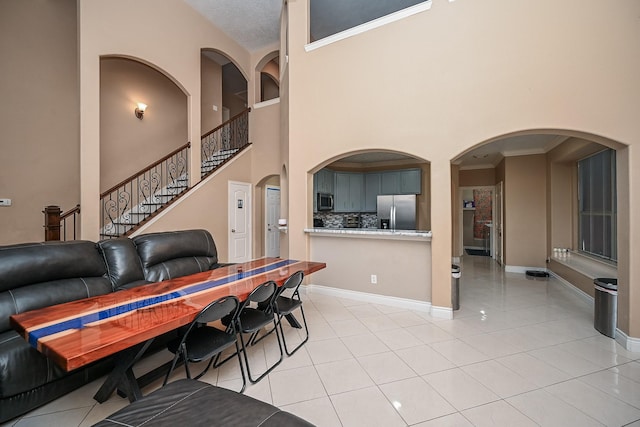 living room featuring stairs, light tile patterned flooring, a towering ceiling, and baseboards