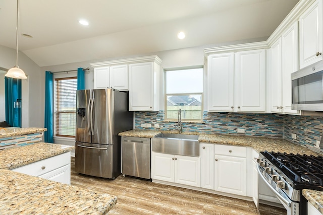 kitchen with stainless steel appliances, a sink, white cabinets, hanging light fixtures, and decorative backsplash