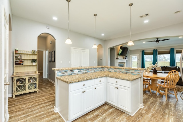 kitchen featuring arched walkways, open floor plan, white cabinets, and decorative light fixtures