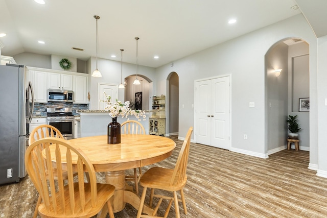 dining area with arched walkways, lofted ceiling, light wood-style flooring, recessed lighting, and baseboards