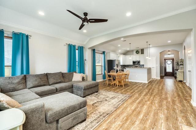 living room with crown molding, arched walkways, vaulted ceiling, and light wood finished floors