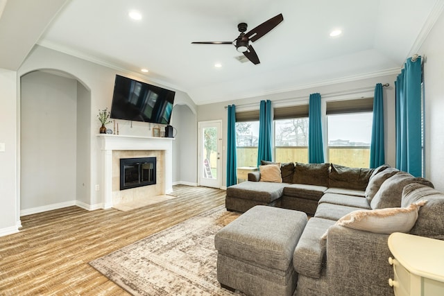 living area with arched walkways, light wood finished floors, a tiled fireplace, ornamental molding, and a ceiling fan