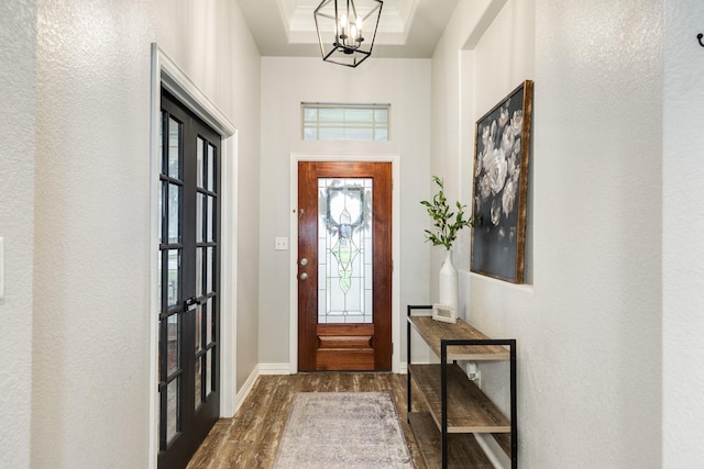 foyer entrance with dark wood-style floors, a tray ceiling, a textured wall, a chandelier, and baseboards