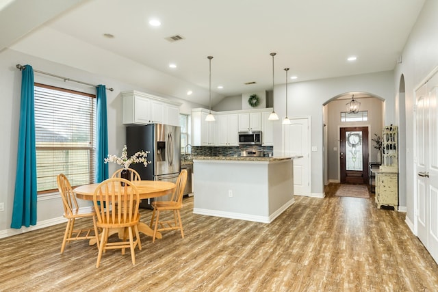 kitchen with stone counters, arched walkways, stainless steel appliances, hanging light fixtures, and white cabinets