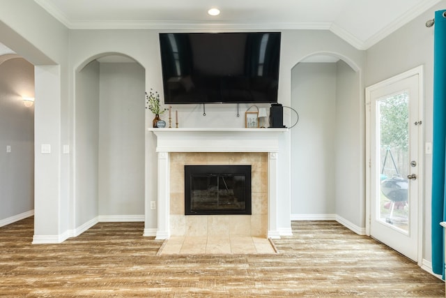 unfurnished living room with light wood finished floors, plenty of natural light, crown molding, and a tiled fireplace