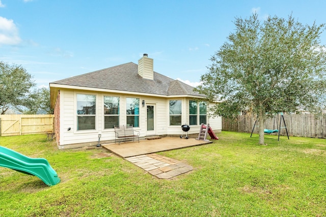 back of property with a chimney, a playground, a yard, and a fenced backyard