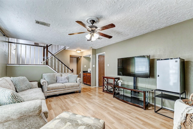 living area featuring light wood finished floors, visible vents, a ceiling fan, stairway, and a textured ceiling