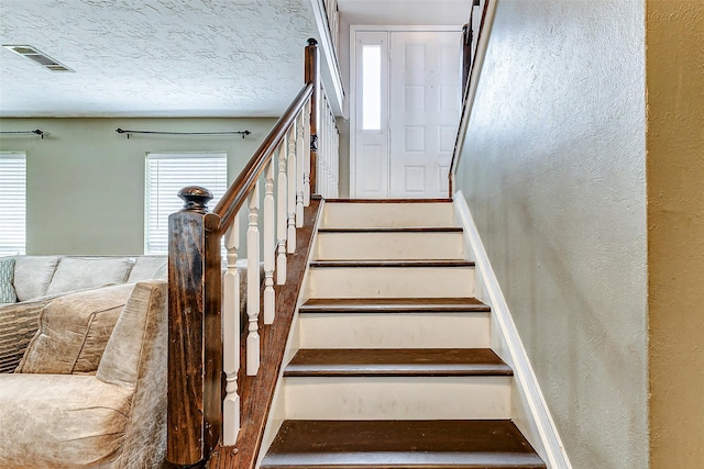 stairway featuring visible vents, a textured wall, and a textured ceiling