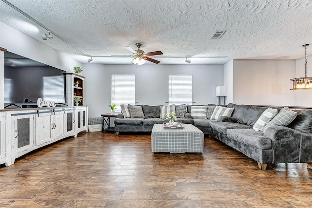 living area with visible vents, dark wood-style flooring, a textured ceiling, track lighting, and ceiling fan with notable chandelier