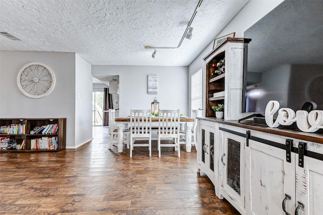 dining space featuring visible vents, dark wood finished floors, a textured ceiling, and track lighting