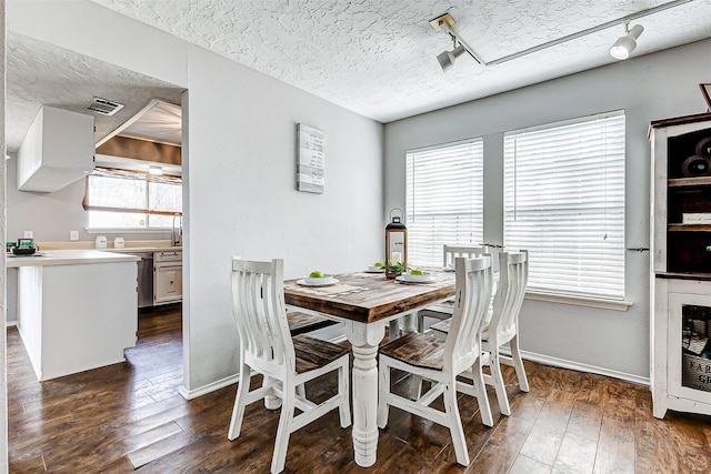 dining area featuring dark wood-type flooring, visible vents, a textured ceiling, and track lighting