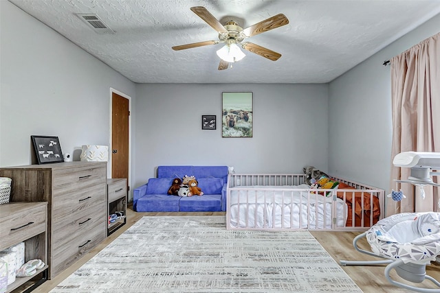 bedroom with a ceiling fan, visible vents, a textured ceiling, and wood finished floors