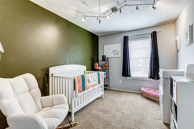 bedroom featuring carpet, rail lighting, a textured ceiling, a nursery area, and baseboards