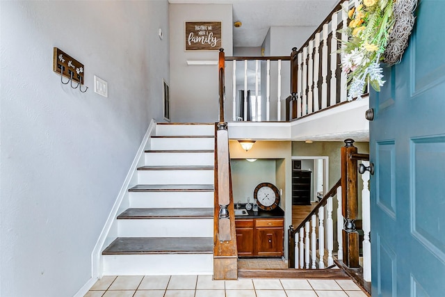 staircase featuring a towering ceiling, baseboards, and tile patterned floors