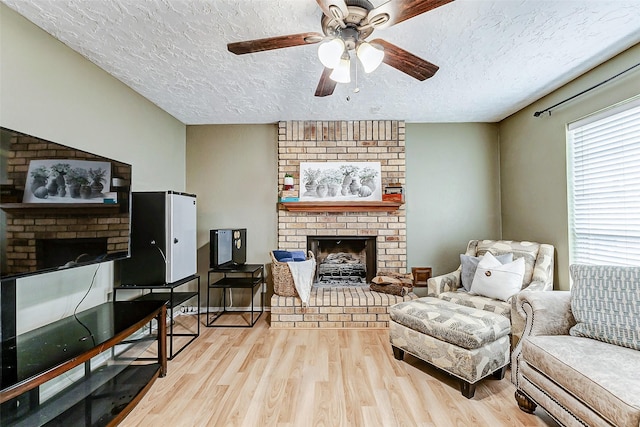 living room with a textured ceiling, ceiling fan, a fireplace, and wood finished floors