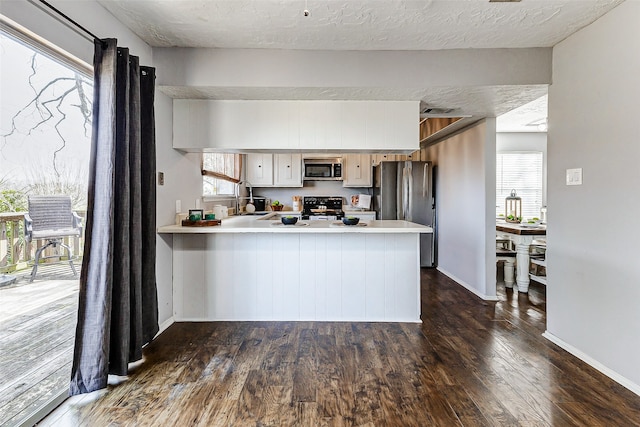 kitchen featuring dark wood-style flooring, a peninsula, stainless steel appliances, light countertops, and white cabinetry