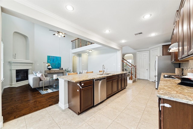 kitchen with open floor plan, a kitchen island with sink, dishwasher, and light stone countertops