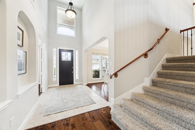 entrance foyer with arched walkways, a towering ceiling, wood finished floors, baseboards, and stairs