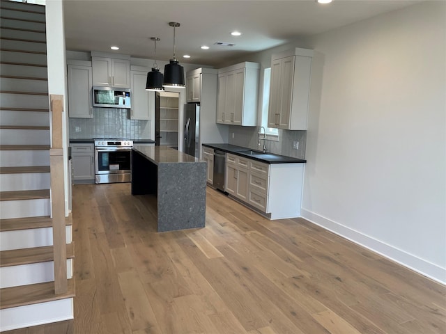 kitchen featuring dark countertops, appliances with stainless steel finishes, a center island, hanging light fixtures, and light wood-style floors