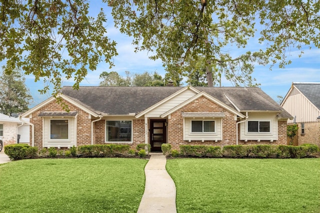 view of front facade with roof with shingles, a front yard, and brick siding