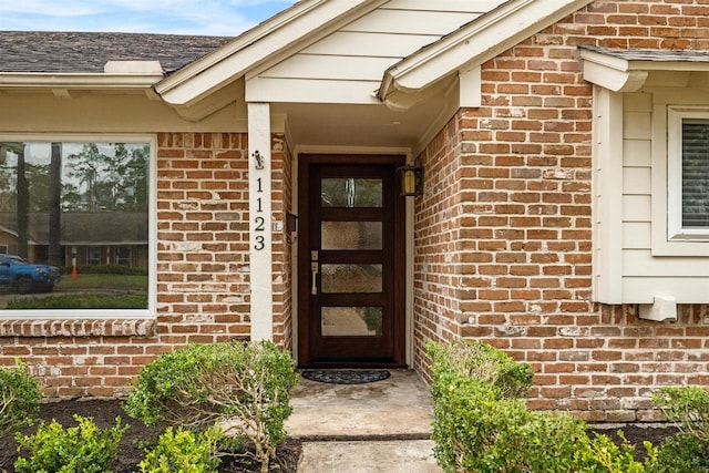 entrance to property featuring brick siding and roof with shingles