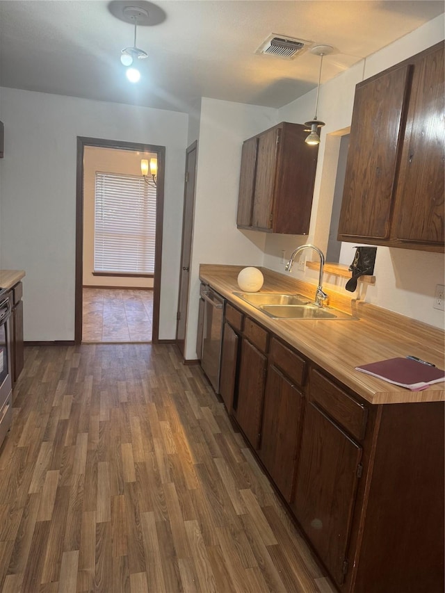 kitchen with dark wood-style flooring, decorative light fixtures, light countertops, stainless steel dishwasher, and a sink