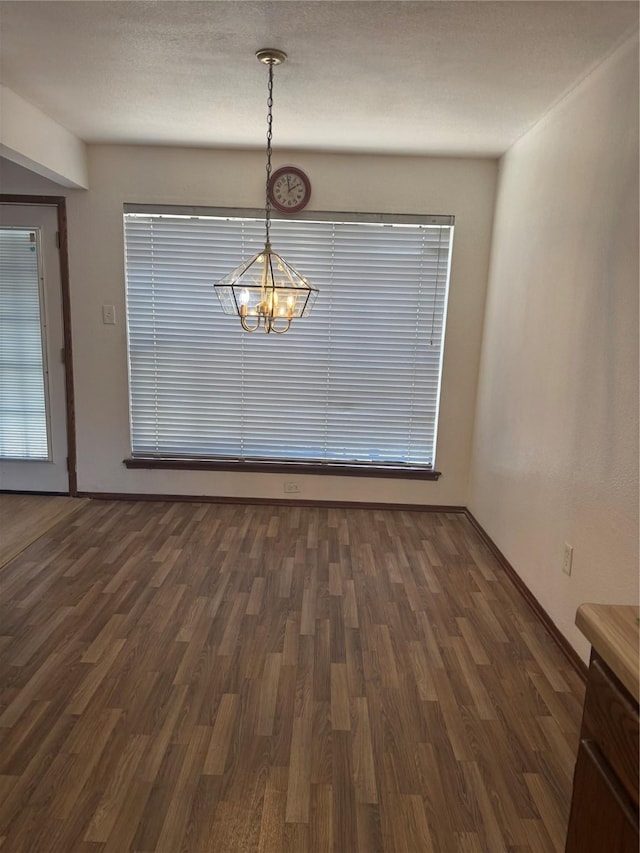 unfurnished dining area featuring baseboards, dark wood finished floors, and an inviting chandelier