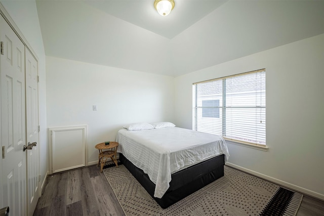 bedroom featuring lofted ceiling, a closet, wood finished floors, and baseboards