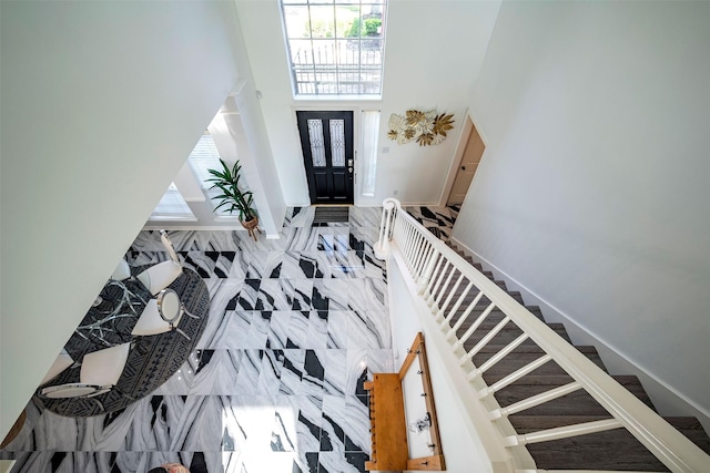 foyer with a towering ceiling, marble finish floor, stairs, and baseboards