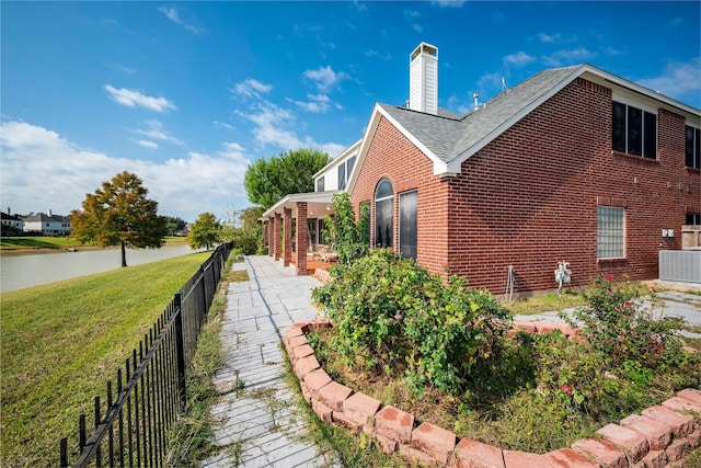 view of side of home with central AC, brick siding, fence, a yard, and a chimney