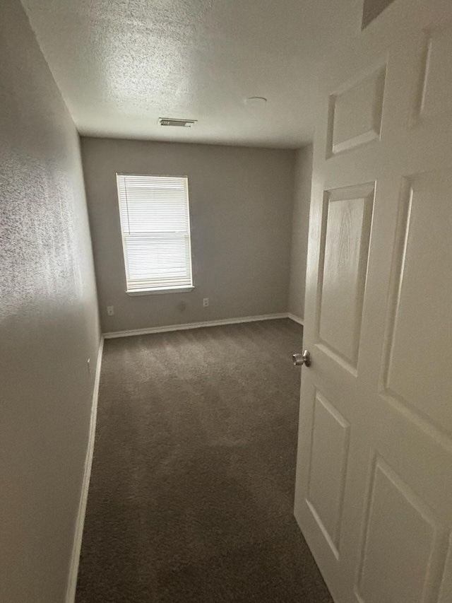 unfurnished room featuring carpet, visible vents, baseboards, and a textured ceiling