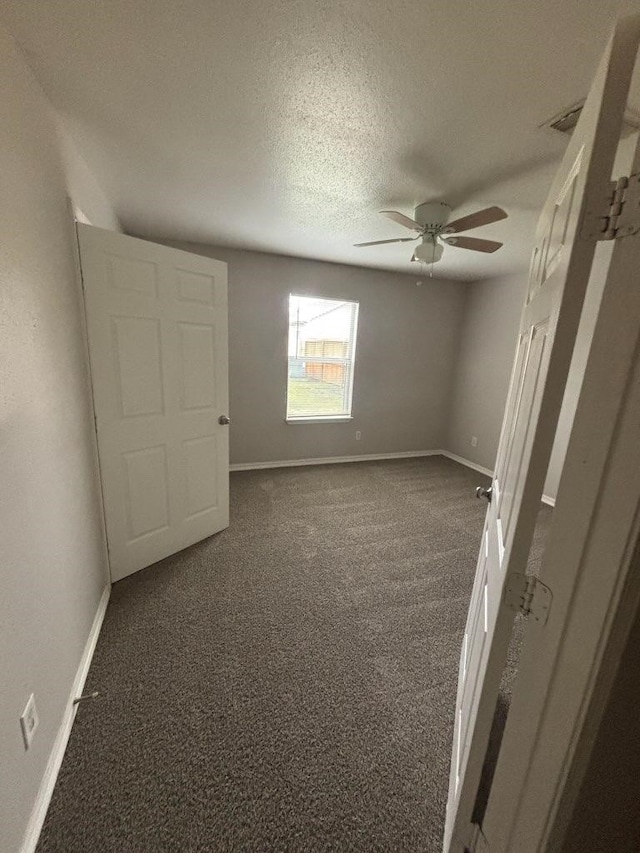 unfurnished bedroom featuring a textured ceiling, dark colored carpet, a ceiling fan, and baseboards