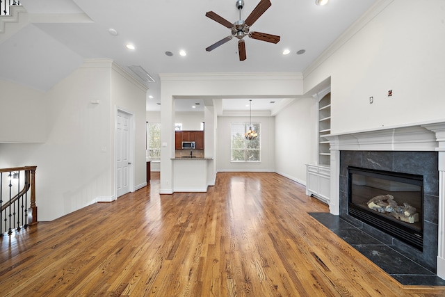 unfurnished living room featuring built in shelves, wood finished floors, a fireplace, recessed lighting, and crown molding