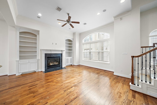 unfurnished living room with visible vents, built in shelves, wood-type flooring, a fireplace, and baseboards