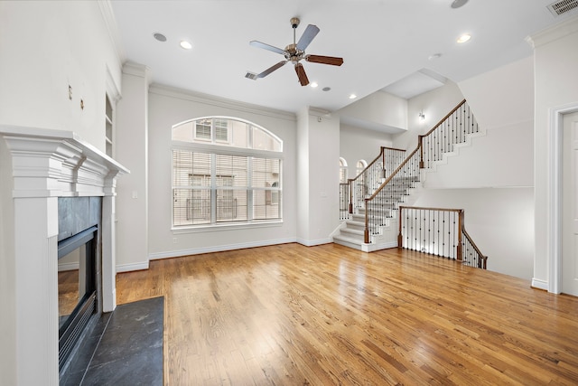 unfurnished living room featuring a tiled fireplace, crown molding, stairway, and wood-type flooring