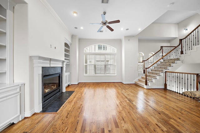 unfurnished living room featuring built in features, light wood-style flooring, a tile fireplace, and stairs