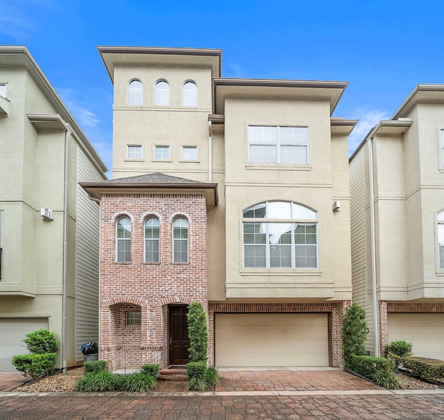 townhome / multi-family property with brick siding, stucco siding, an attached garage, and decorative driveway