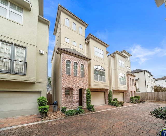 townhome / multi-family property featuring brick siding, fence, stucco siding, decorative driveway, and an attached garage